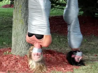 Two girls duct tape mummies outdoors